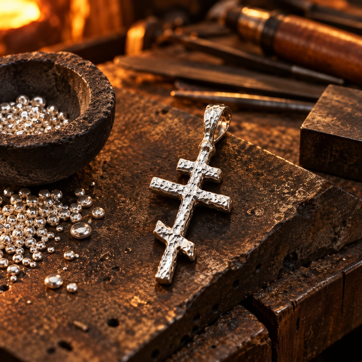 Silver Orthodox Cross Pendant on a silversmith's workbench beside fine silver grain