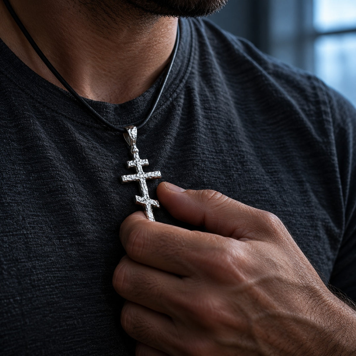 Man holding the silver Orthodox Cross Pendant he wears on a black cord